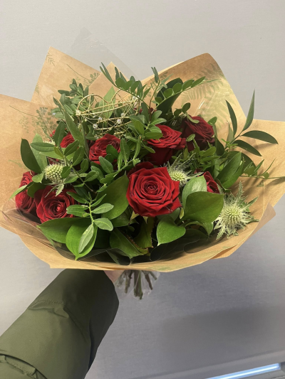 12 Red Roses - 12 Red Roses in a hand-tied bouquet nestled amongst abundant fresh greenery and elegant natural textures. Finished with a delicate heart detail, this stunning arrangement is designed to express deep affection, admiration, and heartfelt sentiment.

Beautifully presented in stylish kraft wrapping, this bouquet is perfect for anniversaries, romantic celebrations, Valentine's Day, or any occasion when words alone are not enough. A timeless gift that conveys love, passion, and appreciation with elegance and charm.