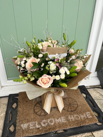 Blush Beauty - A beautifully hand-crafted arrangement in soft blush, ivory and fresh green tones, designed to bring elegance and warmth to any occasion. Delicate seasonal blooms and textured foliage are complemented by shimmering decorative accents, creating a graceful display with a contemporary yet timeless feel. Presented in natural kraft wrapping with a charming ribbon finish, this bouquet is perfect for celebrating special moments, sending thoughtful wishes, or simply brightening someone's day with understated luxury.