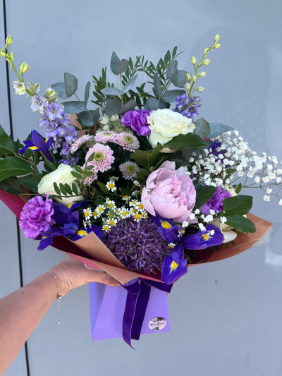 Lavender Skies - A beautifully elegant hand-tied bouquet featuring soft pastel tones, rich violet accents and delicate seasonal textures. Designed with a graceful blend of airy details, lush greenery and romantic blooms, this arrangement captures the serenity of a summer garden in full bloom. Presented in stylish wrapping and finished with a coordinating ribbon, it is a thoughtful choice for birthdays, anniversaries, thank-you gifts, new baby celebrations or simply to brighten someone's day with timeless beauty and charm.