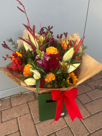 Autumn Glow - A rich and vibrant arrangement inspired by the warmth and colour of the festive season. Bold crimson, golden amber and deep burgundy tones are beautifully complemented by seasonal berries, striking foliage and elegant decorative accents, creating a luxurious display full of texture and character. Presented in a stylish gift bag with rustic wrapping and a statement red bow, this bouquet is perfect for Christmas celebrations, winter birthdays, seasonal gatherings or sending festive cheer to someone special. A truly eye-catching design that captures the magic of the season.